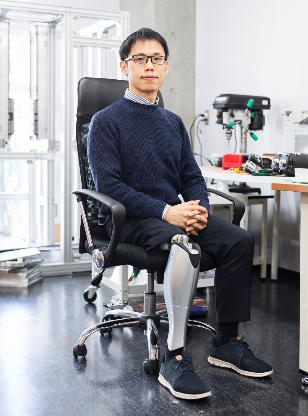 Sun from BionicM Inc. sitting in a chair while wearing a robotic leg prosthesis